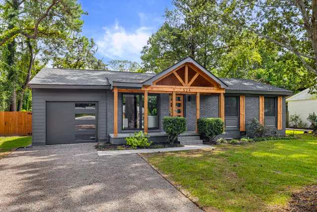 Gray-brick ranch with a cedar timber porch gable, cedar posts, a frosted-glass garage door, and a manicured lawn.